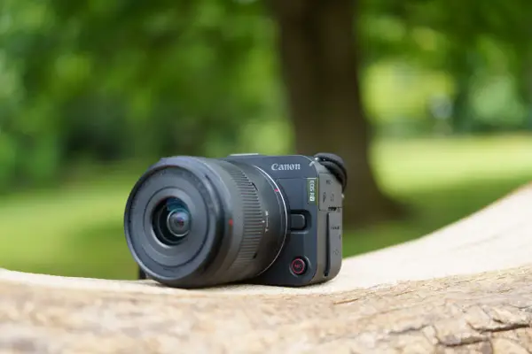 Un appareil photo Canon EOS R50, prêt pour un test en extérieur. Le soleil brille sur son objectif.