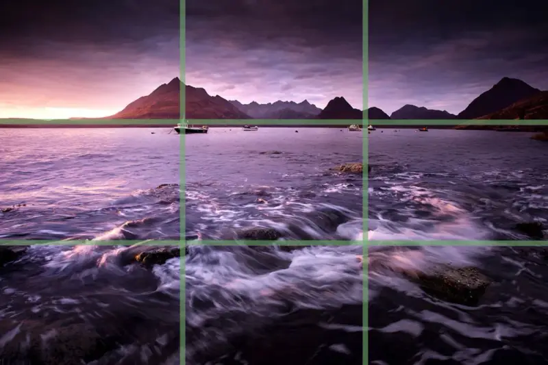 Paysage marin au crépuscule, avec des montagnes en arrière-plan et des bateaux sur l'eau. La composition suit la règle des tiers pour un équilibre visuel.
