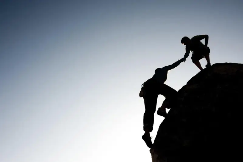 Silhouette d'un grimpeur aidant un autre à atteindre le sommet. Une belle présentation photographe de l'entraide et de la persévérance.